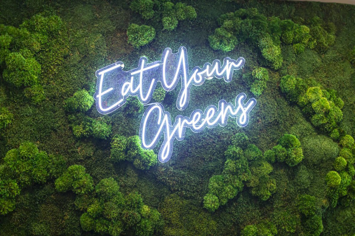 neon sign with the words "eat your greens" on top of a green landscape background