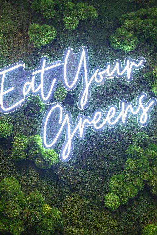 neon sign with the words "eat your greens" on top of a green landscape background