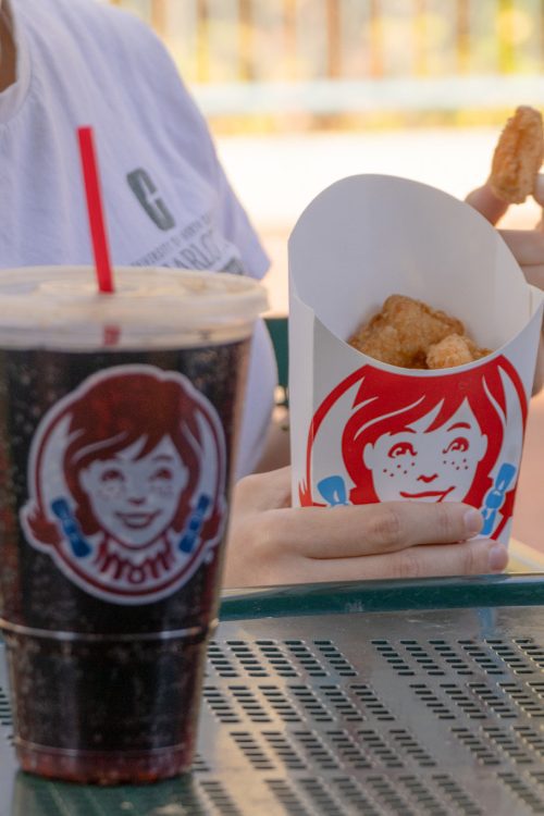 Wendy's soft drink cup on table in front of a student eating from a box of Wendy's chicken nuggets