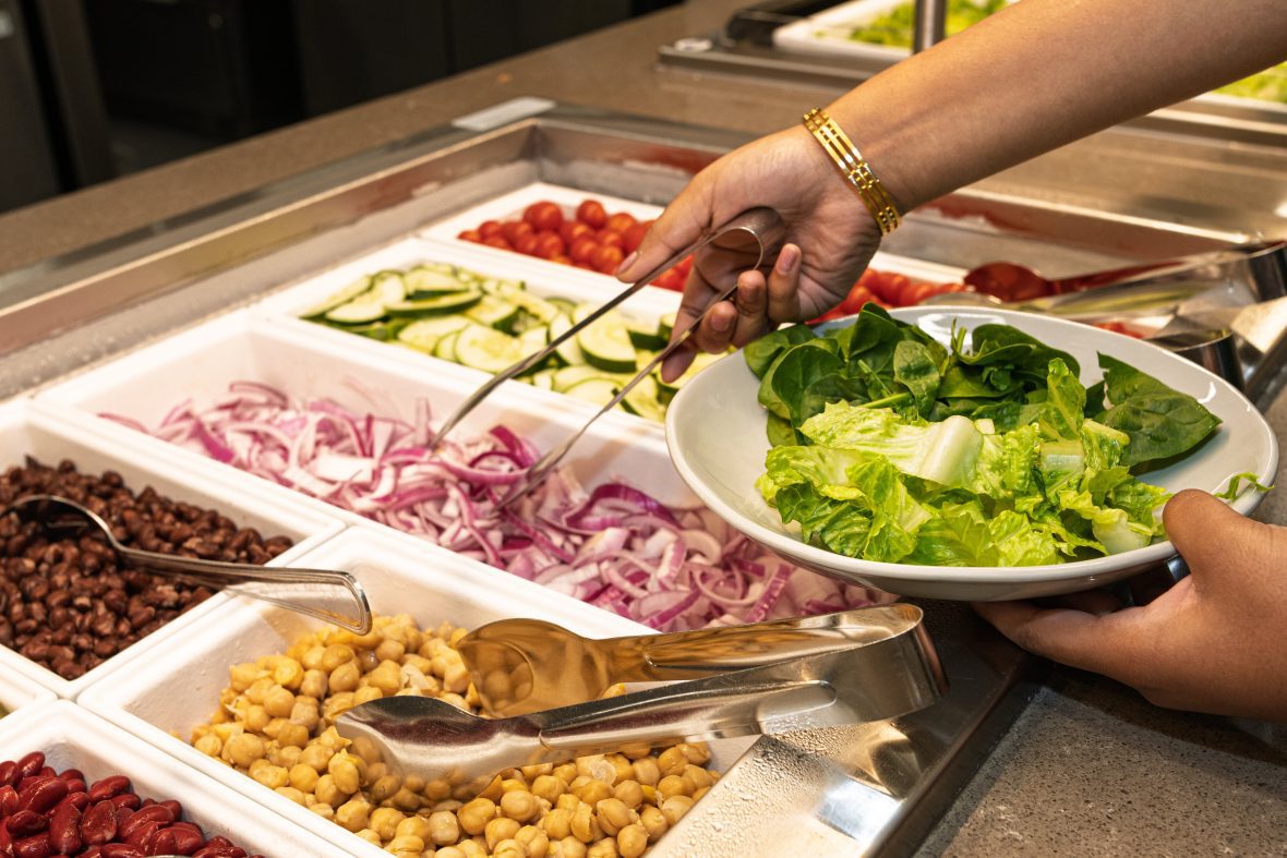 Hand with tongs filling plate at a salad bar