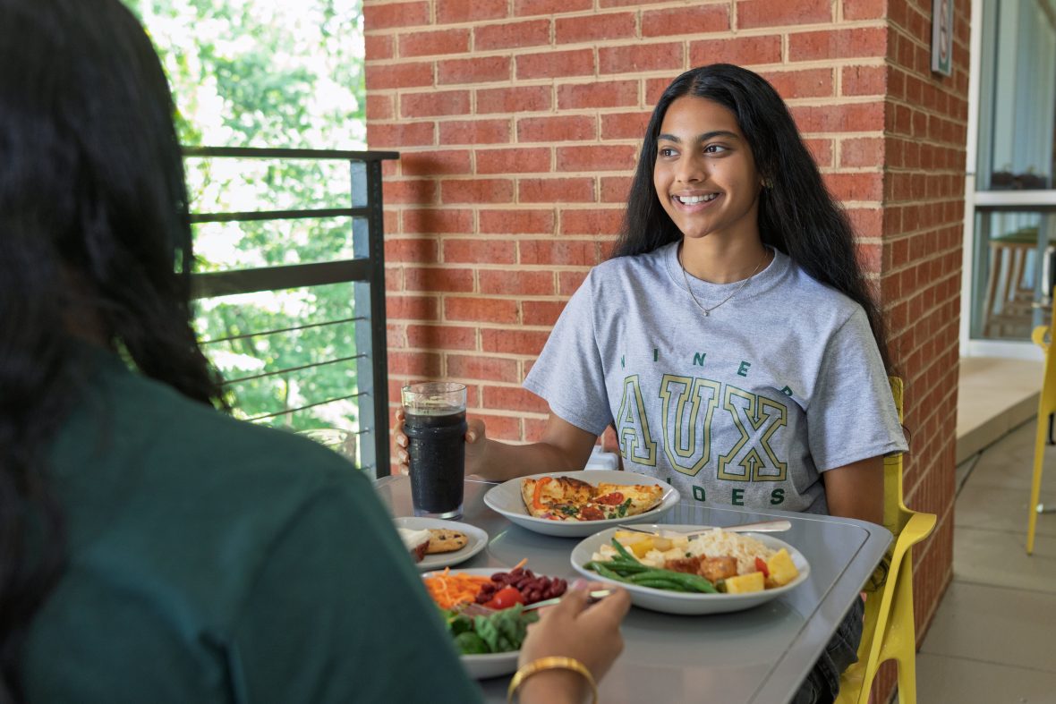 Smiling student on dining hall patio with plates of food on table.