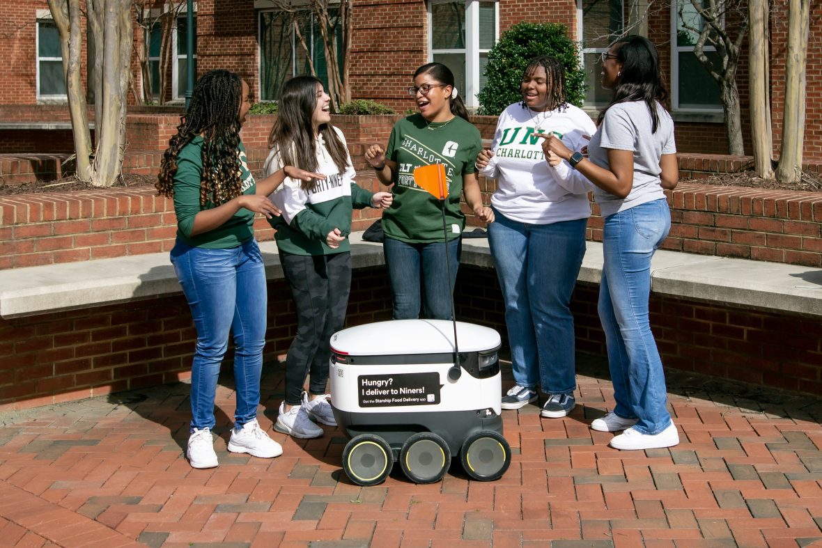A group of students standing around a starship delivery robot.
