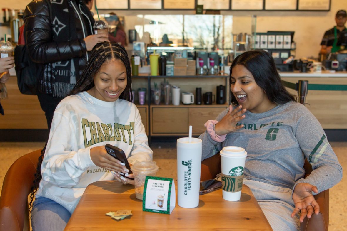 Two students with drinks in a library Starbucks, looking at a phone