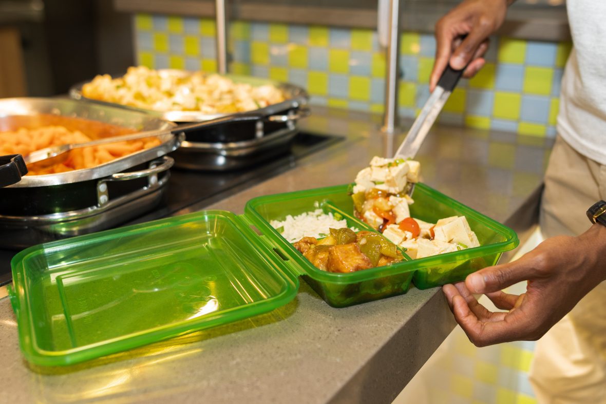 Student adding tofu and vegetables into green, reusable takeout container