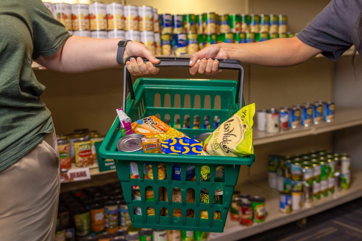 Two people holding a shopping basket of pantry food items