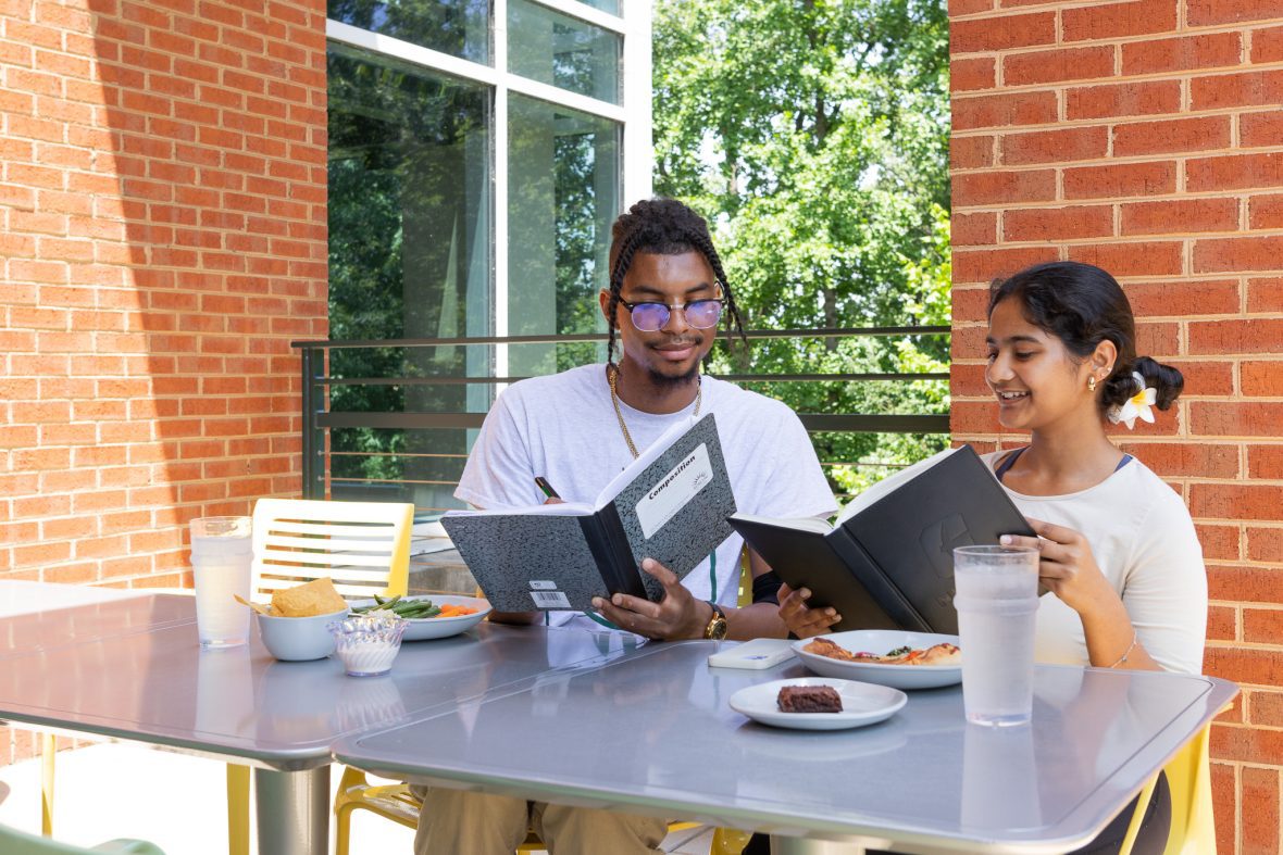 Students sitting at table outside with plates of food and looking at notebooks