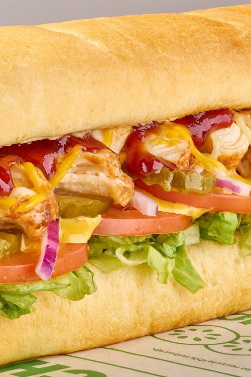 Sub sandwich with chicken, sauce and vegetables inside white bread