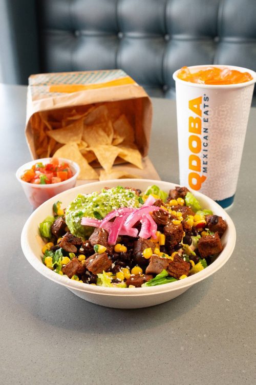 Burrito bowl with meat, black beans, and vegetables. Bag of tortilla chips, pico, and fountain drink in background